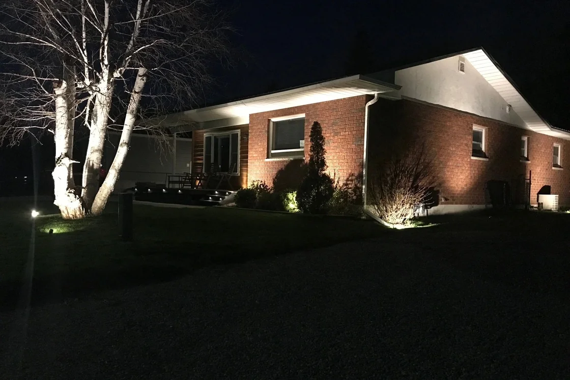 A brick house at night with landscape uplighting on a birch tree and washes of light along the eaves.