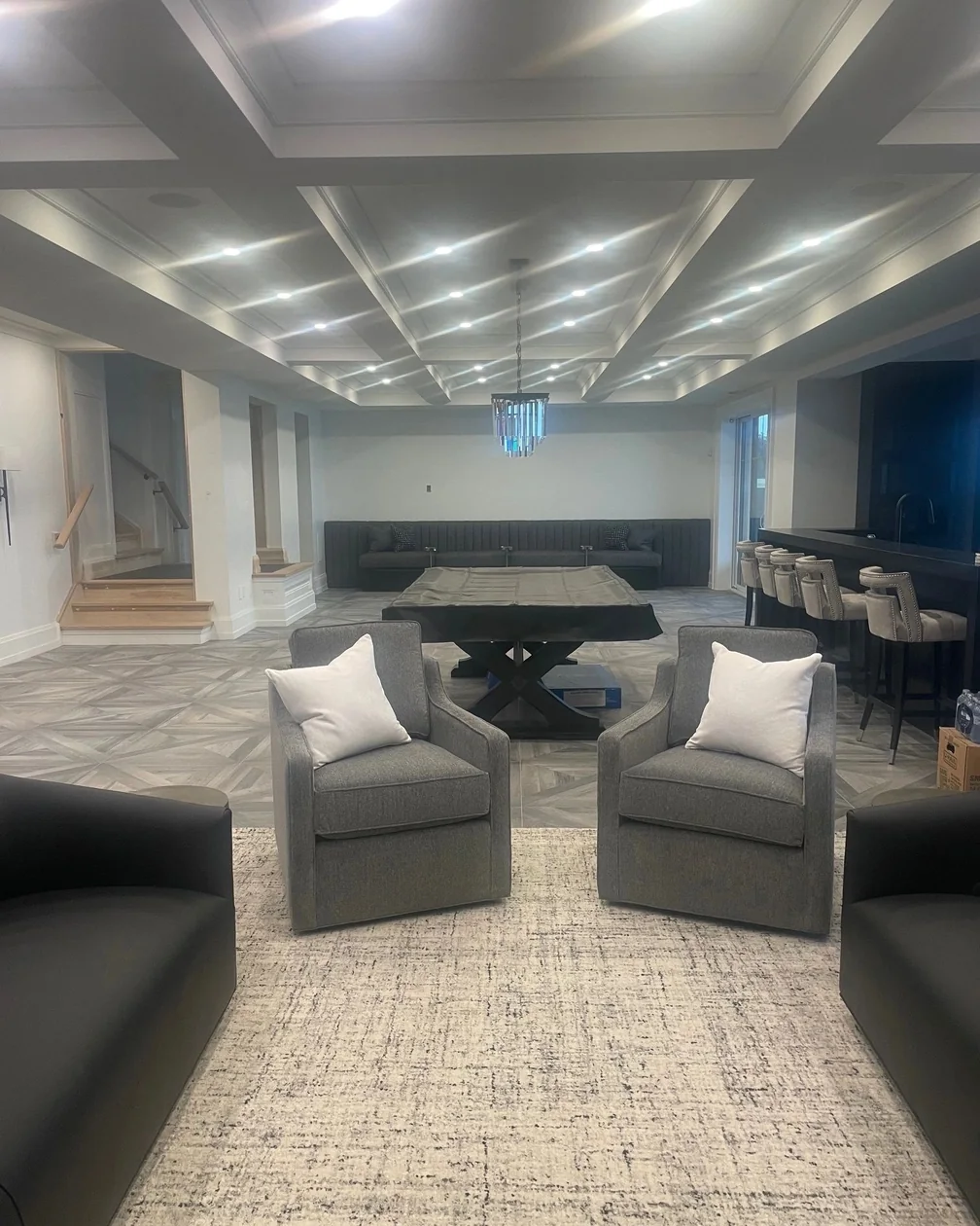 A finished basement with a coffered ceiling full of recessed lights and a chandelier over a pool table.
