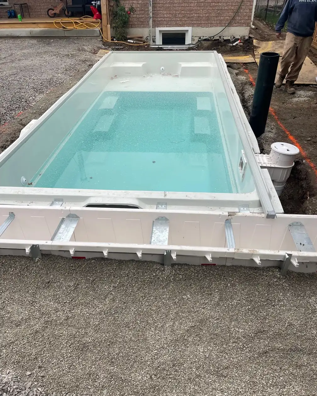 A swim spa being installed in a concrete deck, with conduit and rough-in visible at the edge.