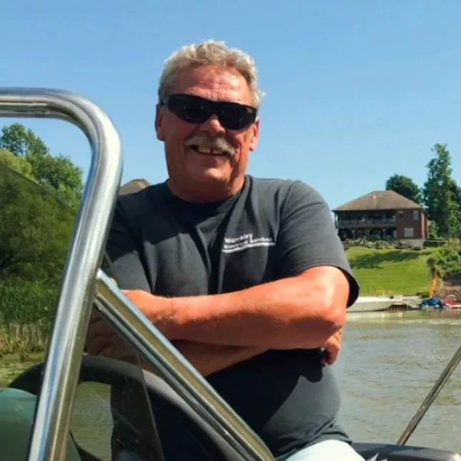 A man in sunglasses leaning on the rail of a boat on a sunny day.