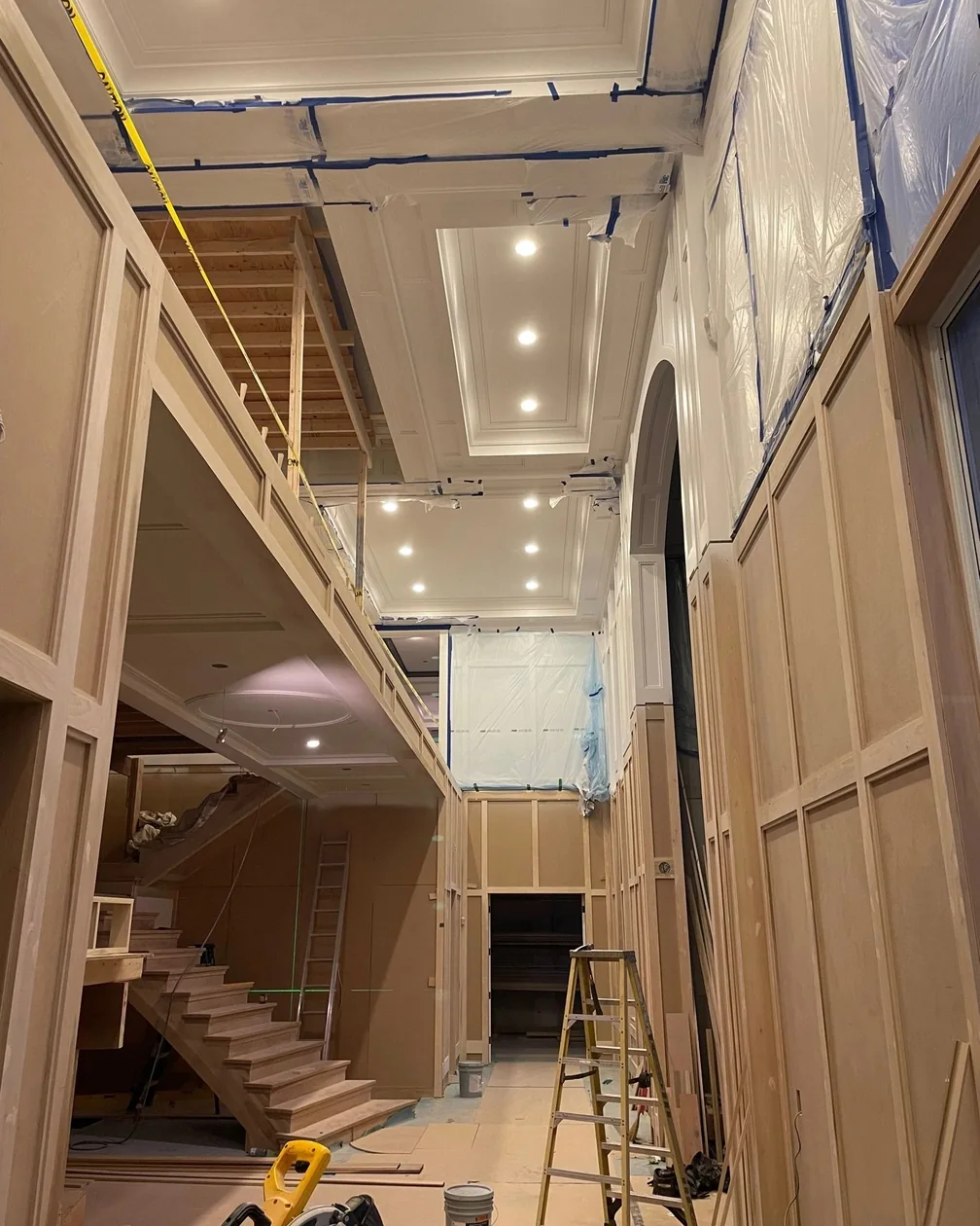 A high end interior under construction, with a coffered ceiling full of recessed lights above a staircase and bare framing still visible.