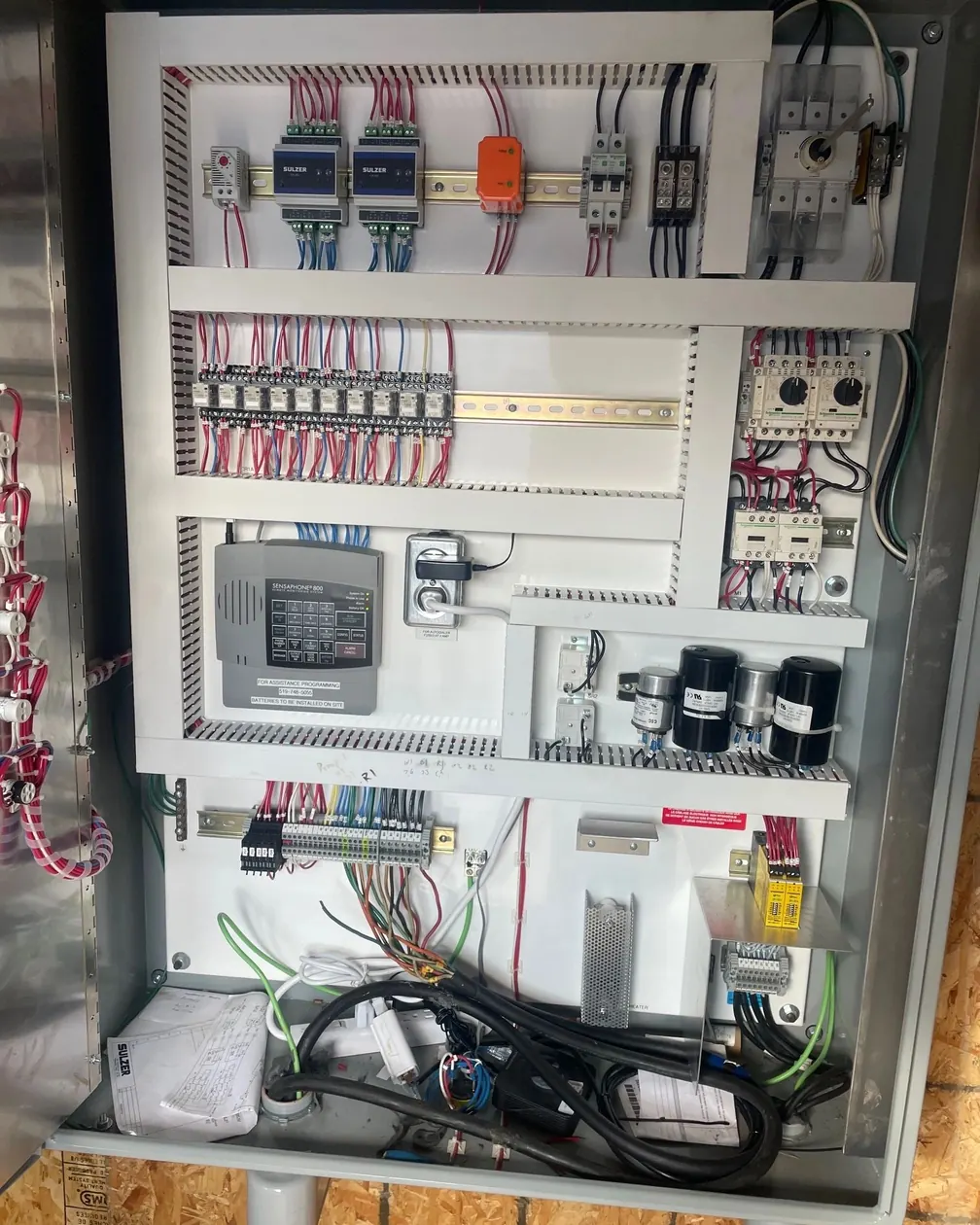 An open industrial control panel showing DIN rail mounted relays, a controller, terminal blocks and numbered wiring.