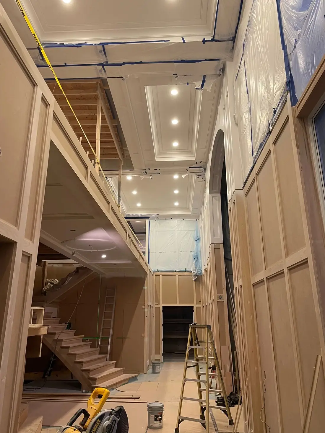 A high end interior under construction, with a coffered ceiling full of recessed lights above a staircase and bare framing still visible.