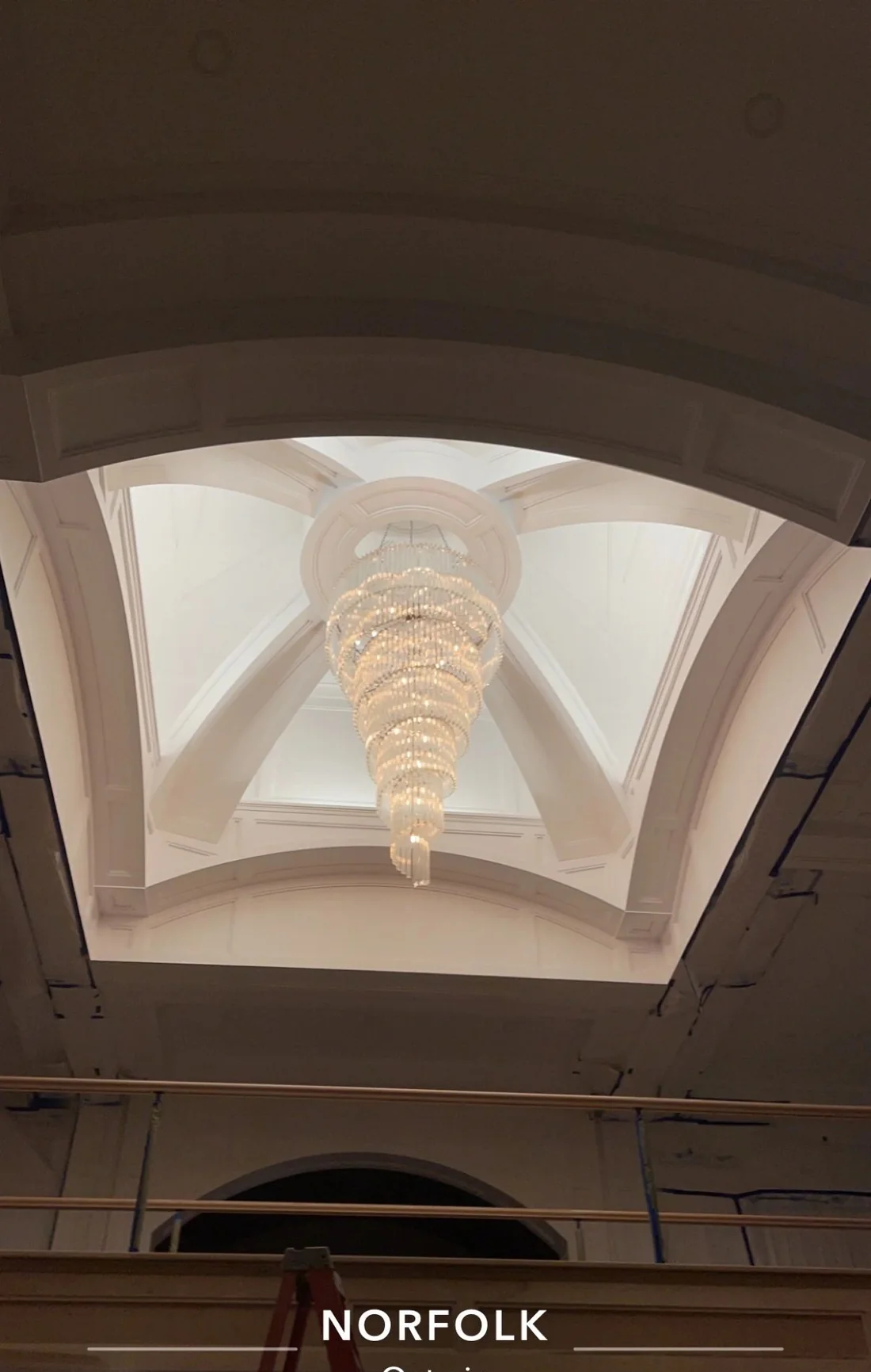 A barrel vaulted ceiling with a chandelier, still under construction with a ladder in frame.
