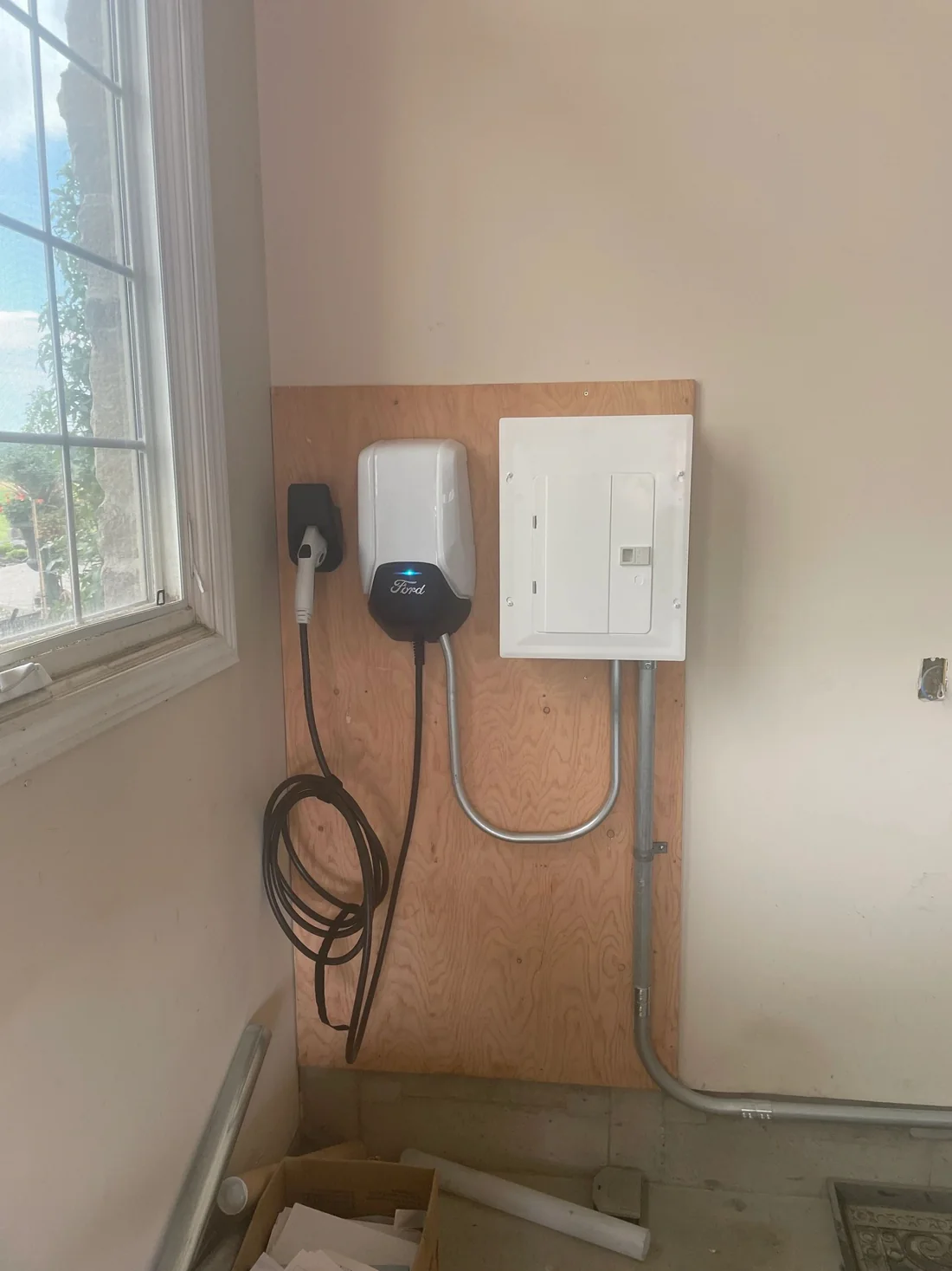 An EV charger mounted on a plywood wall with conduit running to a panel.
