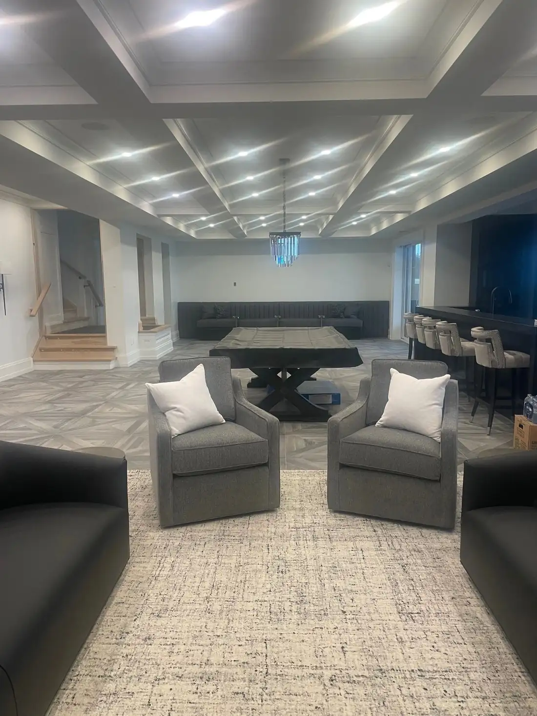 A finished basement with a coffered ceiling full of recessed lights and a chandelier.