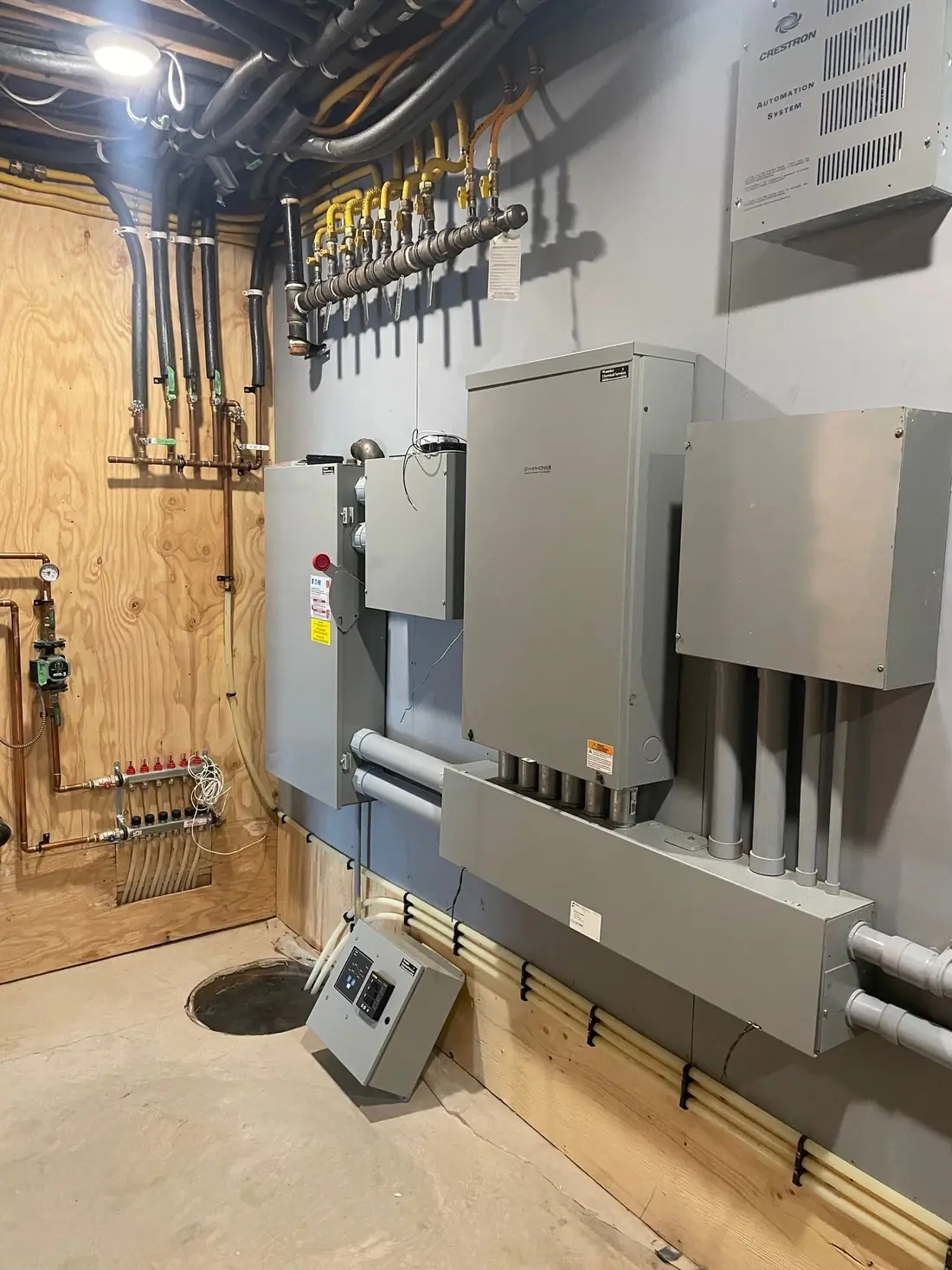 A mechanical room wall with grey electrical panels, conduit and a manifold.