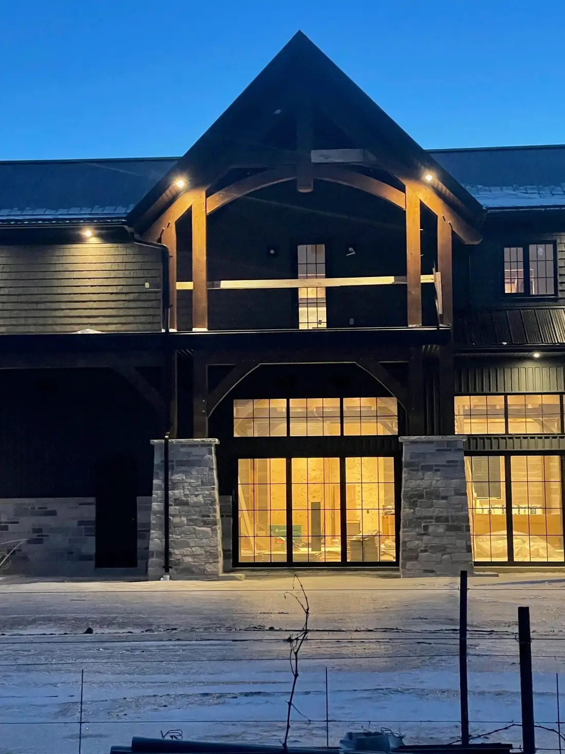 A large timber frame house at dusk with warm light through tall windows.