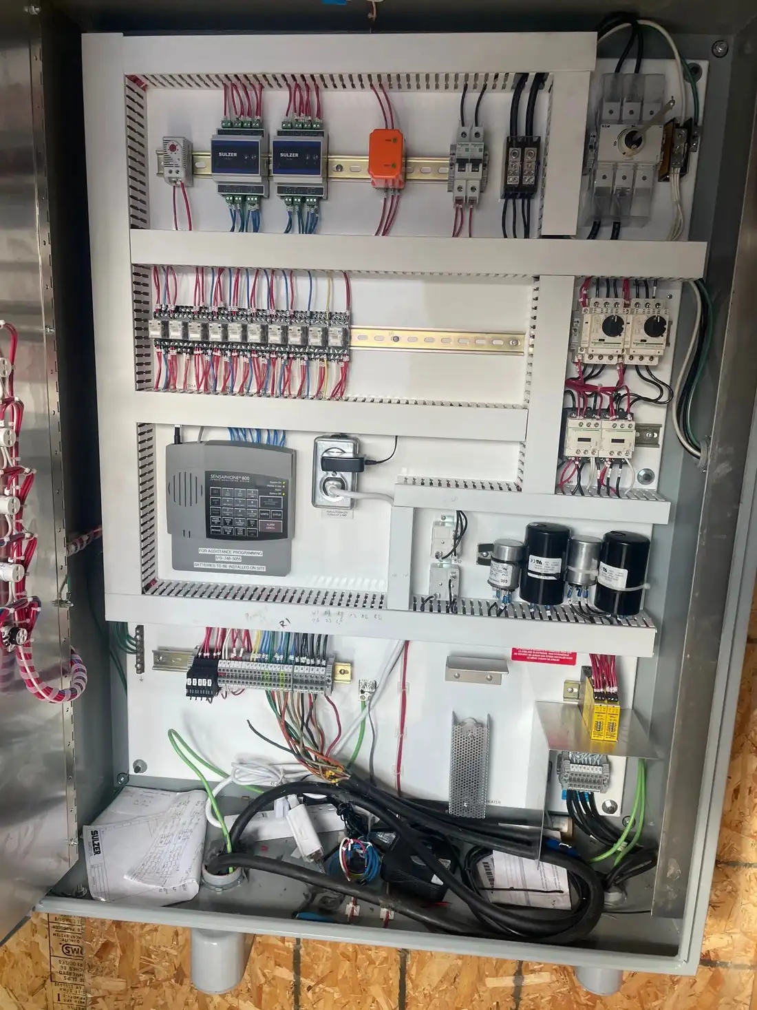 An open industrial control panel showing DIN rail mounted relays, a controller, terminal blocks and numbered wiring.