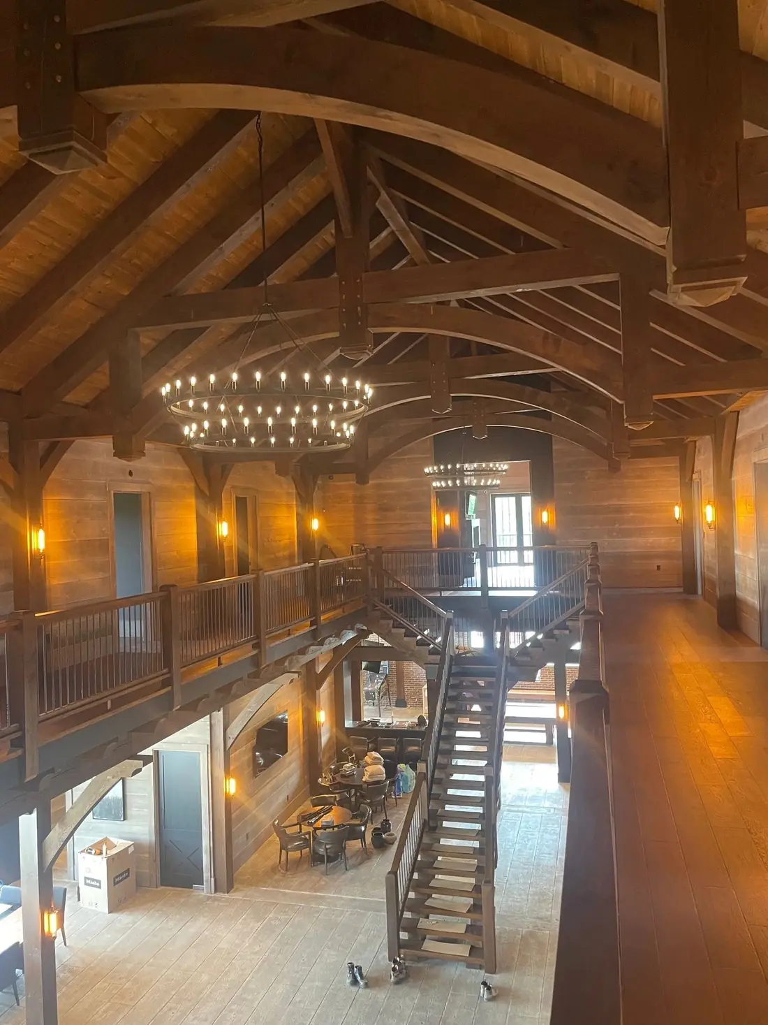 A timber frame great room with an exposed truss roof and a circular chandelier.