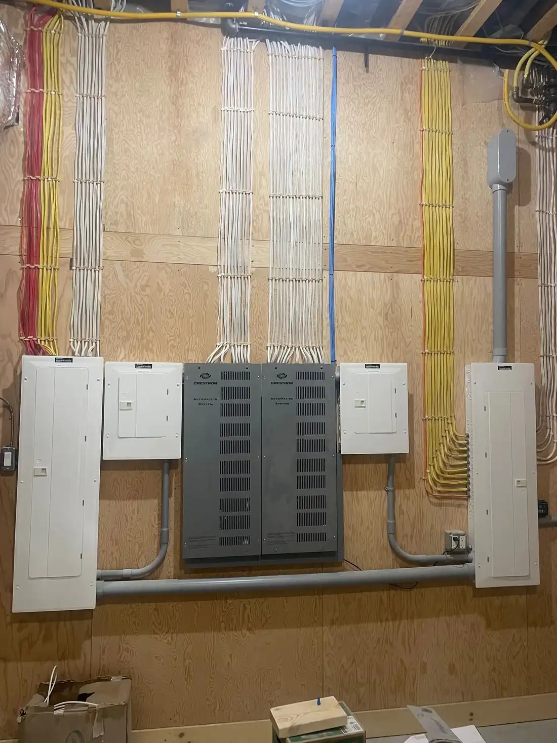 A rough-in wall with a main panel and sub panels, and dozens of home run cables dressed in neat parallel runs.